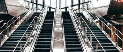 A set of symmetrical modern escalators offering parallel paths up and down inside a brightly lit building.