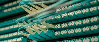 A close-up view of teal fiber optic cables neatly plugged into a high-tech data center server rack.