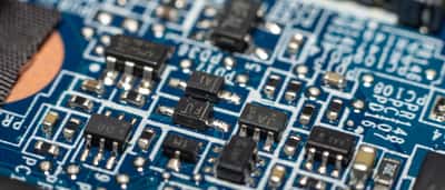 A close-up macro view of a blue electronic circuit board with various surface-mounted components.