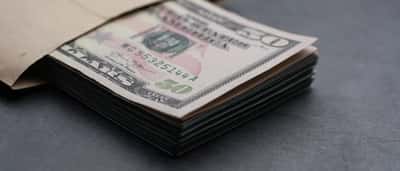 A thick stack of US fifty dollar bills resting partially inside a plain brown envelope on a dark surface.