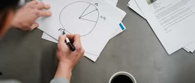 A person's hands drawing and dividing a pie chart with a marker on a piece of paper.