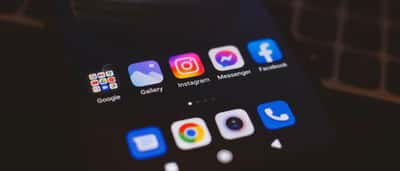 A smartphone screen glows in the dark, displaying popular social media applications including Instagram, Messenger, and Facebook.