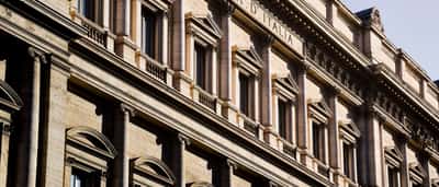 The grand, sunlit neoclassical stone facade of the Banca d'Italia building in Rome.