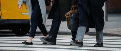 A crop of professionals carrying briefcases as they cross a downtown city street.
