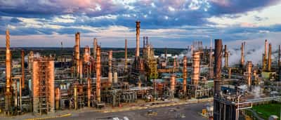 An aerial view of a massive oil refinery complex illuminated under a dramatic sunset sky.