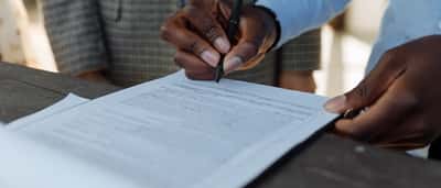Close-up of business professionals formally signing a corporate document with a pen at a desk.