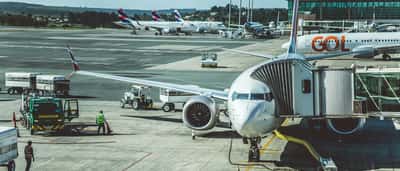 A commercial Boeing 737 MAX airplane parked at an airport gate while ground crew and vehicles prepare it for its next flight.