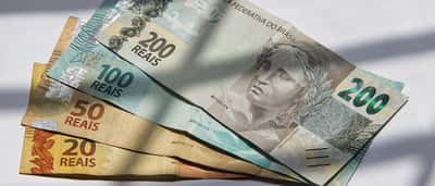 Brazilian real banknotes are displayed in bright sunlight with contrasting diagonal shadows.