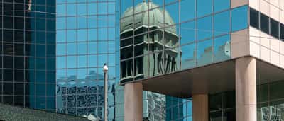 A historic classic building with a dome is reflected in the sleek blue glass windows of a modern skyscraper.