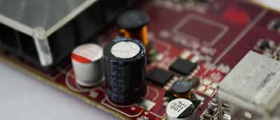 A close-up macro view of a black cylindrical capacitor and other electronic components mounted on a red computer circuit board.