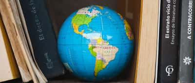 A colorful world globe sits on a wooden bookshelf between classic volumes.