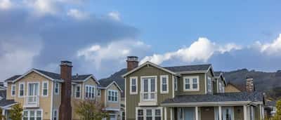 Modern, upscale suburban houses line a residential street under a blue and cloudy sky.