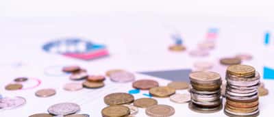 A neat stack of coins resting on printed financial charts and data.