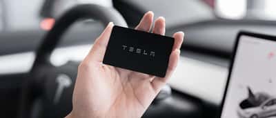 A hand holds a black Tesla key card inside the modern interior of a vehicle.