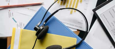 A customer service headset resting on colorful folders and printed financial charts.