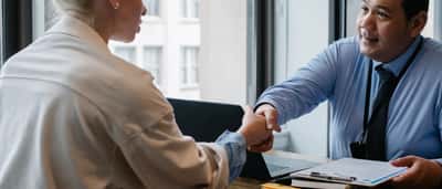 A smiling manager shakes hands with a candidate across a desk in a bright, modern office.