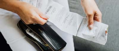 Close-up of a person's hands reviewing multiple store receipts pulled from a black wallet.