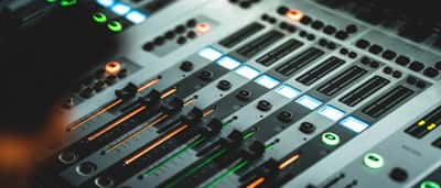 Close-up of a modern audio mixing console with illuminated sliders and dials.