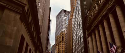 The classic facade of the New York Stock Exchange building stands alongside towering skyscrapers in the dense urban canyon of Wall Street.