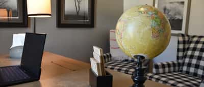 A world globe, a laptop, and wooden calendar blocks sit on a desk in a warm, modern office setting.