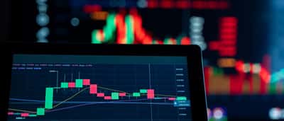 A digital trading chart is displayed on a screen in sharp focus, with a larger, brightly lit chart blurred in the background.