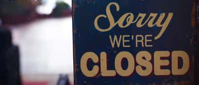 A rustic 'Sorry We're Closed' sign hangs on the glass door of a shop.