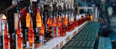 Glowing hot glass bottles move along an automated production line in a manufacturing plant.