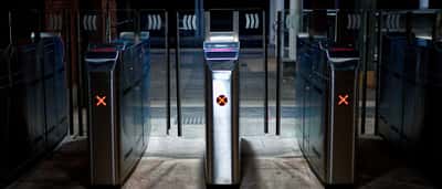 Illuminated modern subway turnstiles displaying bright red crosses in a dark station, indicating entry is blocked.