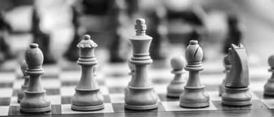 Black and white close-up of wooden chess pieces facing each other on a chessboard.