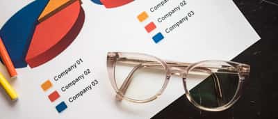 Transparent eyeglasses rest on a printed document displaying colorful pie charts and a legend detailing company allocations.