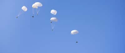 Multiple white parachutes safely lowering cargo boxes through a clear blue sky.