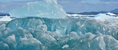 A large, textured blue iceberg floats in the water with its submerged layers visible beneath the surface.