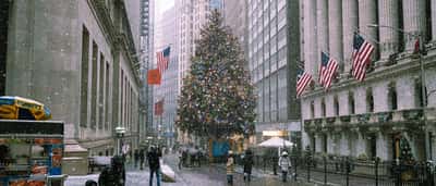 A large decorated Christmas tree stands outside the New York Stock Exchange building during a winter snowfall.