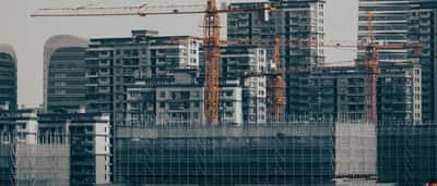 Multiple construction cranes tower over unfinished high-rise buildings surrounded by scaffolding in a Chinese city.