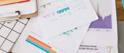 Printed financial documents and charts scattered on a desk, including a graph tracking the S&P 500 index.