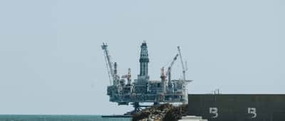 An offshore oil rig stands in the ocean under a clear blue sky.