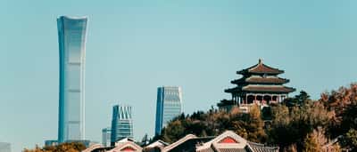 Traditional Chinese architecture in the foreground contrasts with the modern skyscrapers of Beijing's central business district rising against a clear blue sky.