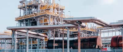 An oil refinery complex with metal pipelines stands behind black transport tanker wagons.