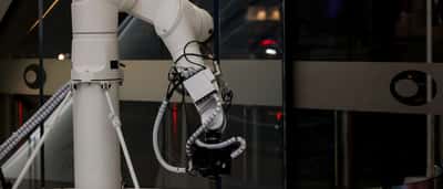 A sleek, modern white robotic arm operates inside a contemporary glass-walled building.