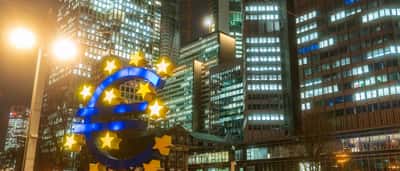 The illuminated Euro sculpture stands in front of office buildings at night in Frankfurt, Germany.