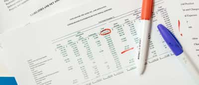 A printed financial statement detailing functional expenses lies on a desk alongside a red marker and a blue pen.