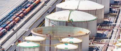 Aerial view of massive white industrial oil storage tanks alongside roads and railway tracks.