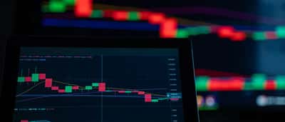 A digital screen displays a cryptocurrency trading chart with prominent red candlestick patterns indicating a market decline.