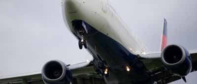 A Delta Air Lines passenger jet flies overhead against an overcast sky.