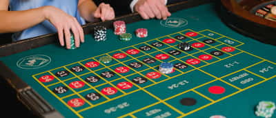 People place stacks of chips on a green casino roulette table.
