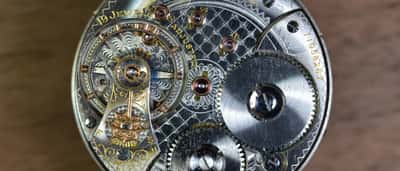 A detailed macro view of an intricate silver and gold watch mechanism with exposed gears and jewels.
