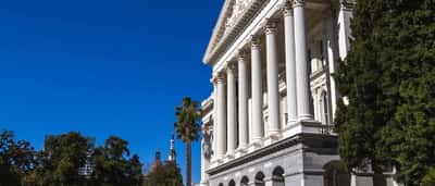 A brightly lit state capitol building with classic white columns against a clear blue sky.