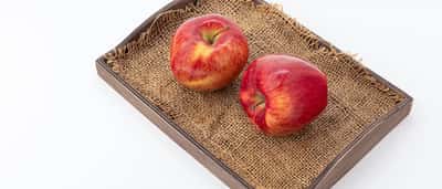 Two identical red apples sit side by side on a wooden tray.