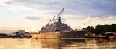 A modern U.S. Navy warship docked in a serene harbor bathed in golden sunset light.