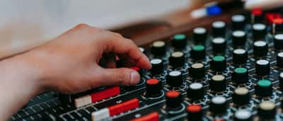 A person's hand adjusts the illuminated knobs and sliders on a professional sound mixing console.
